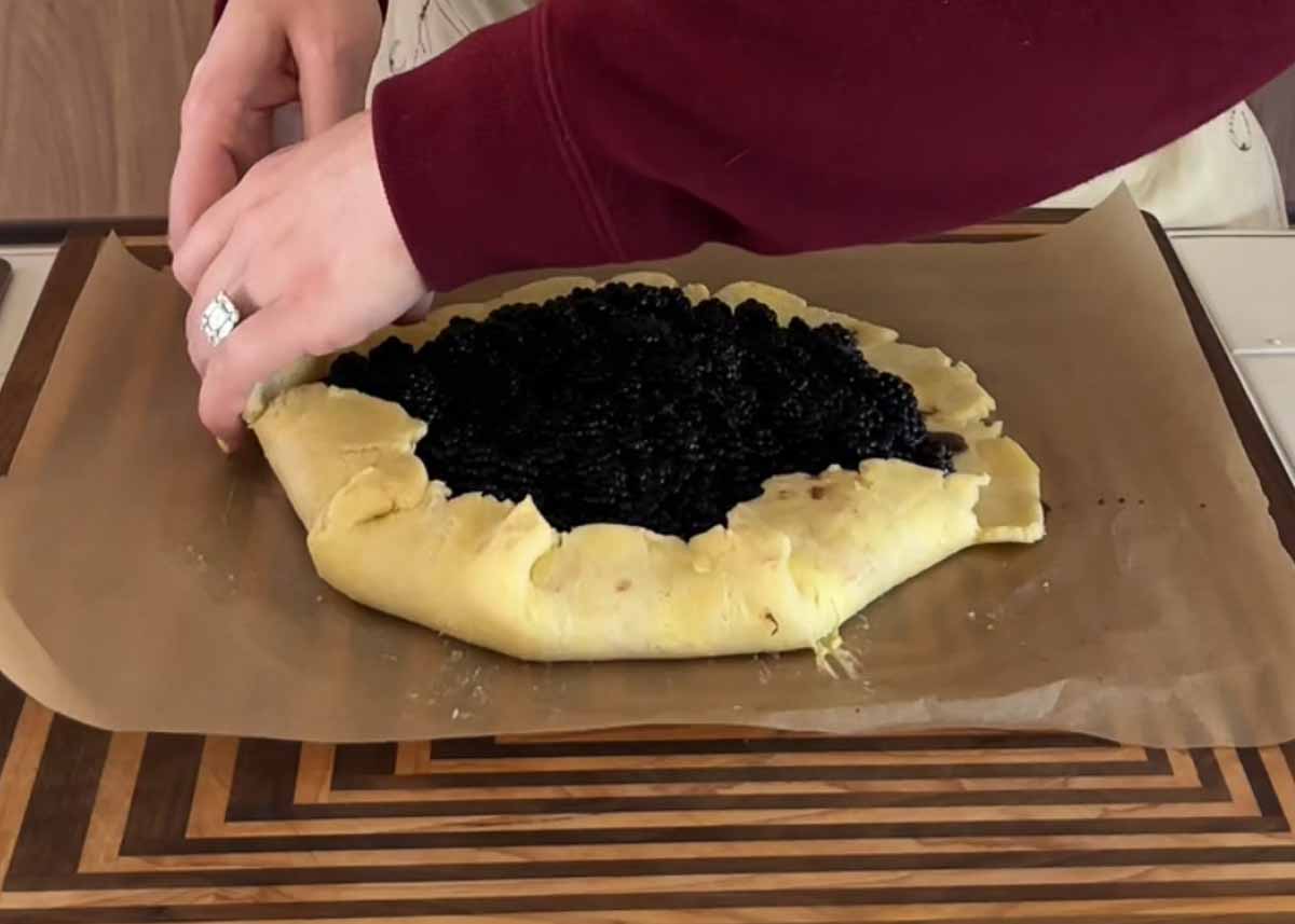 Hands folding pastry over blackberry filling to shape a rustic galette.