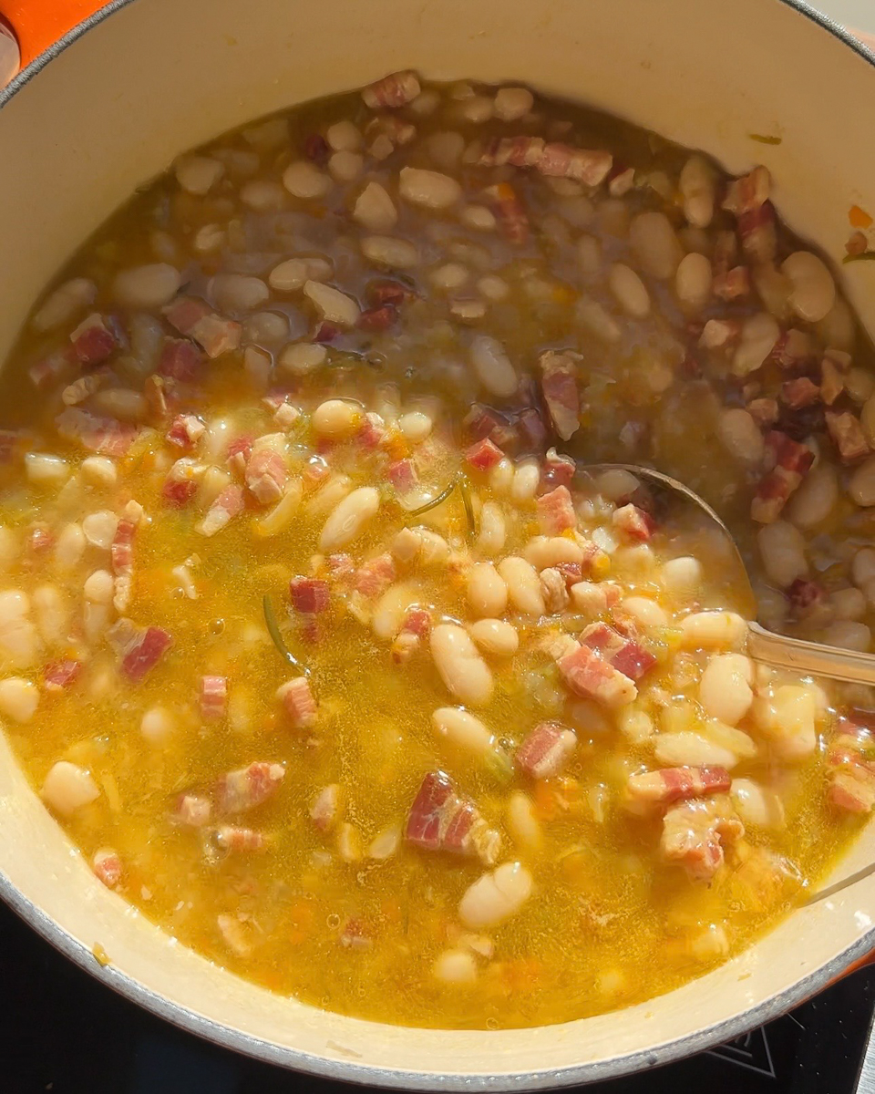 Italian white bean and pancetta soup served in a rustic bowl with olive oil and herbs.