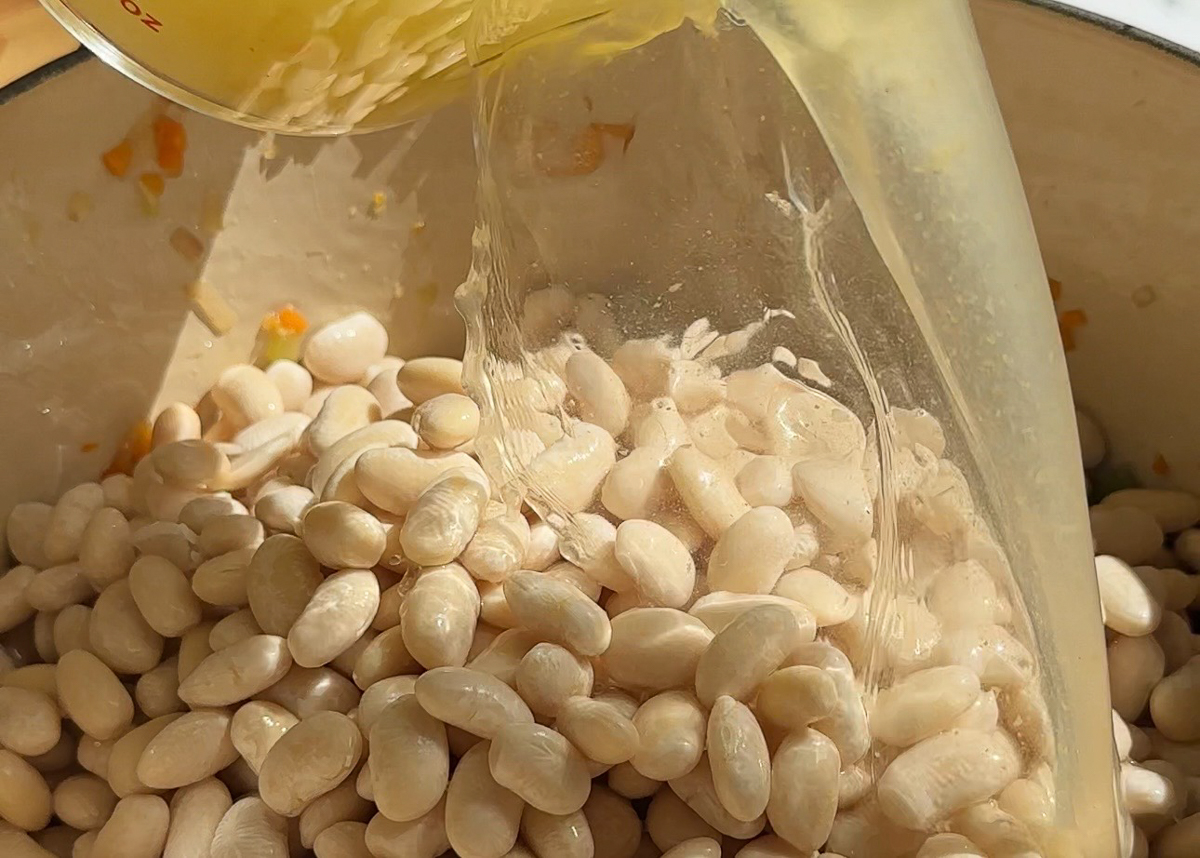 Stock being poured over great Northern beans in pot for Italian bean soup