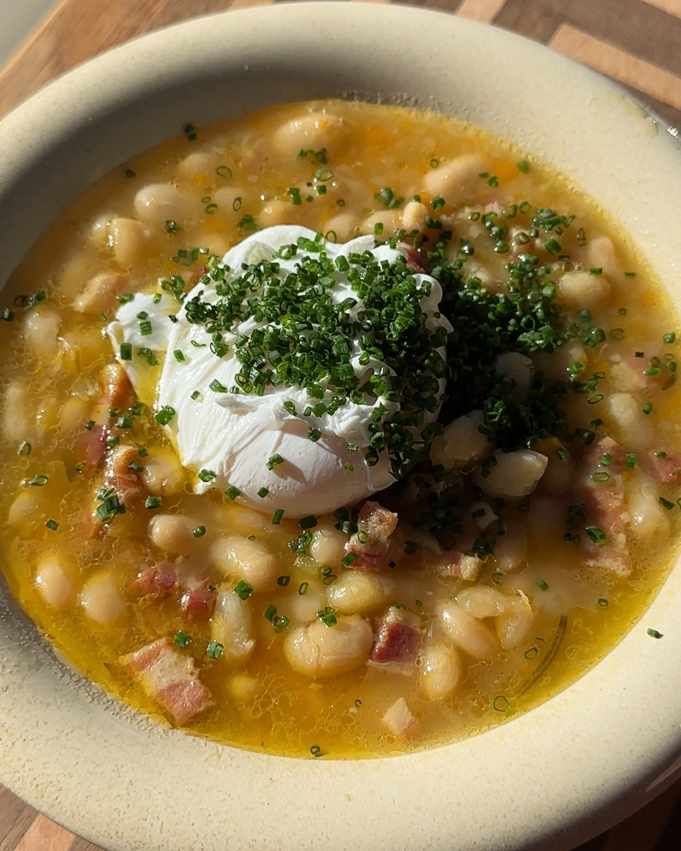 Tuscan white bean and pancetta soup topped with a soft poached egg and fresh chives in a shallow bowl