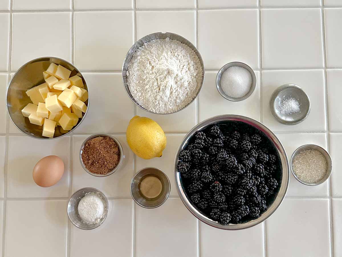 Ingredients for wild blackberry galette including fresh blackberries, butter, flour, sugar, lemon and eggs on a kitchen bench.