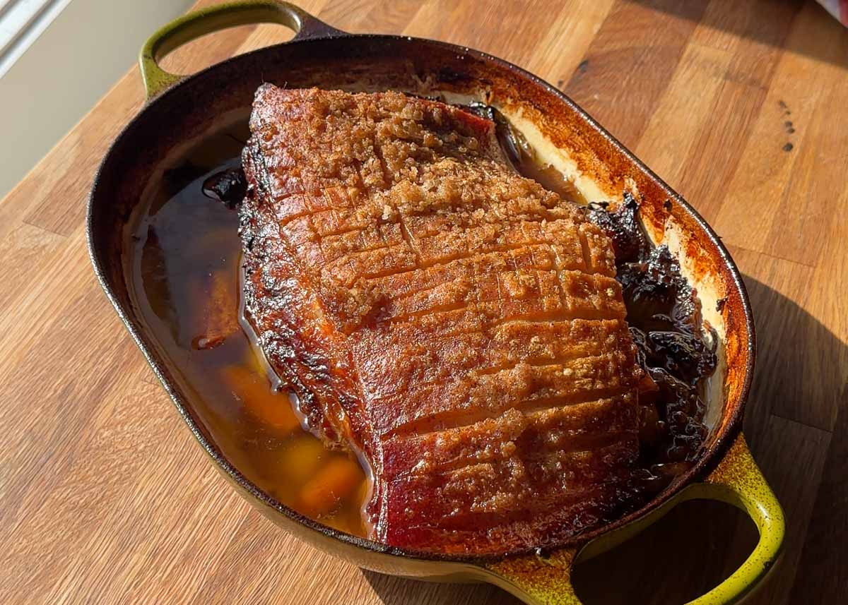 Beer braised pork shoulder in a roasting dish with cooking juices and crispy crackling