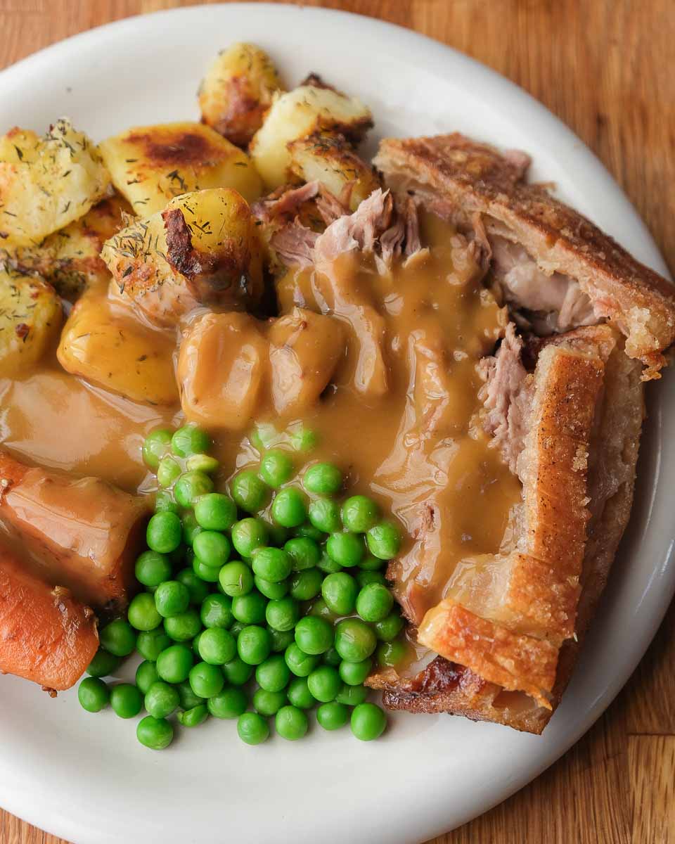 Slow cooked pork shoulder with crackling served with roasted potatoes and vegetables