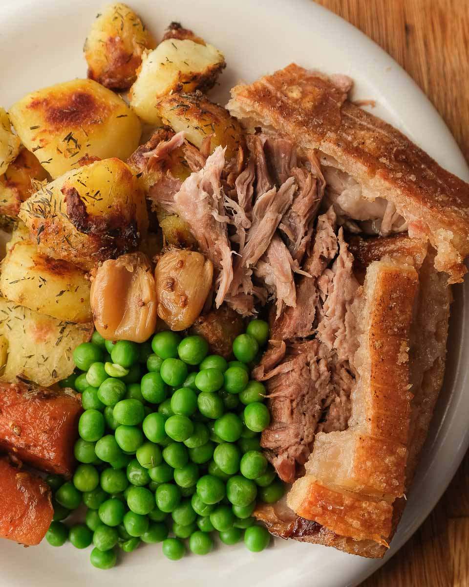 Beer braised pork shoulder served as a roast dinner with potatoes, peas and carrots