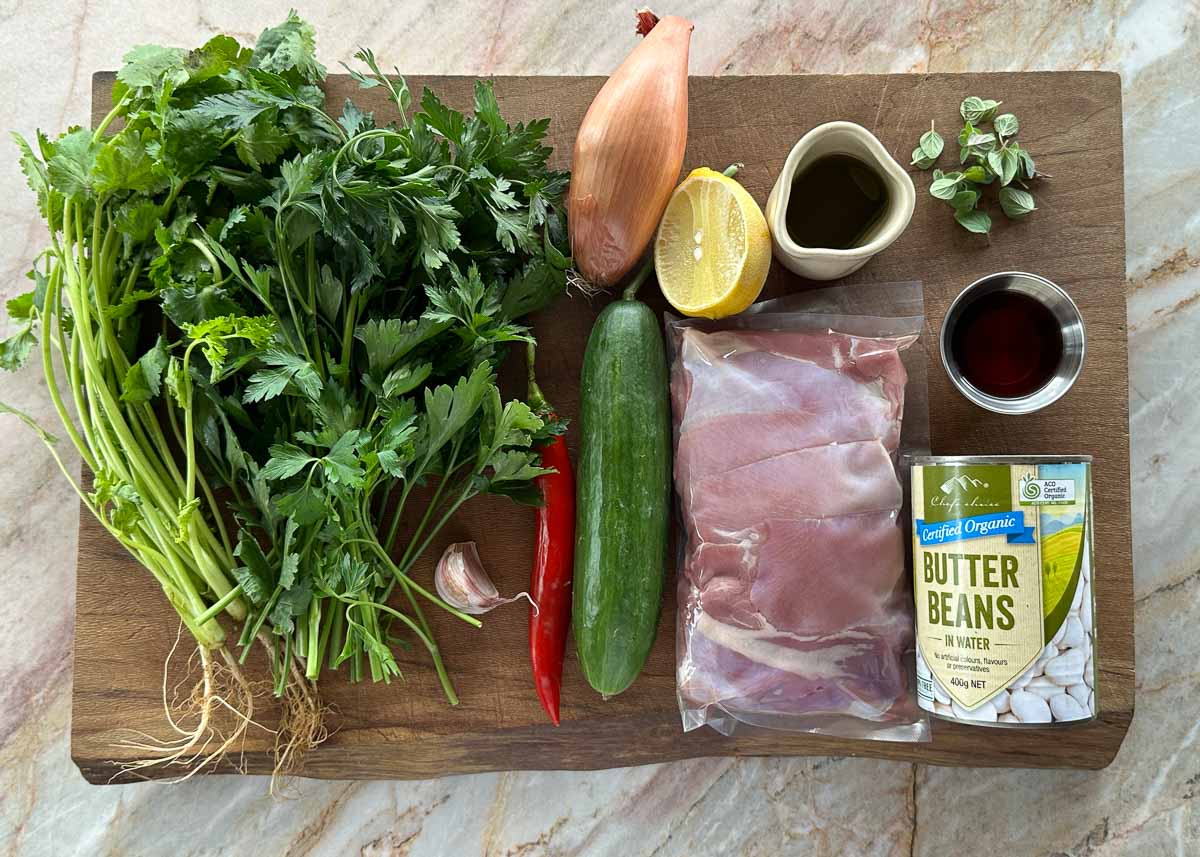 Ingredients for grilled chicken with chimichurri butter bean salad including fresh herbs, cucumber and chicken thighs