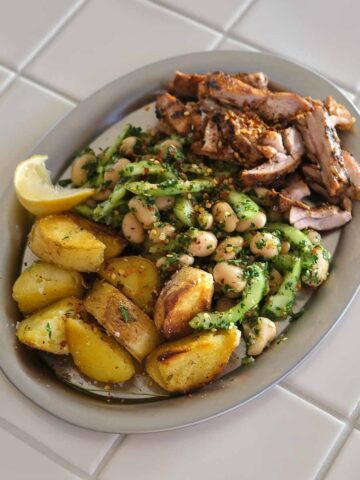 Grilled chicken with chimichurri butter bean salad and crispy potatoes served on a plate