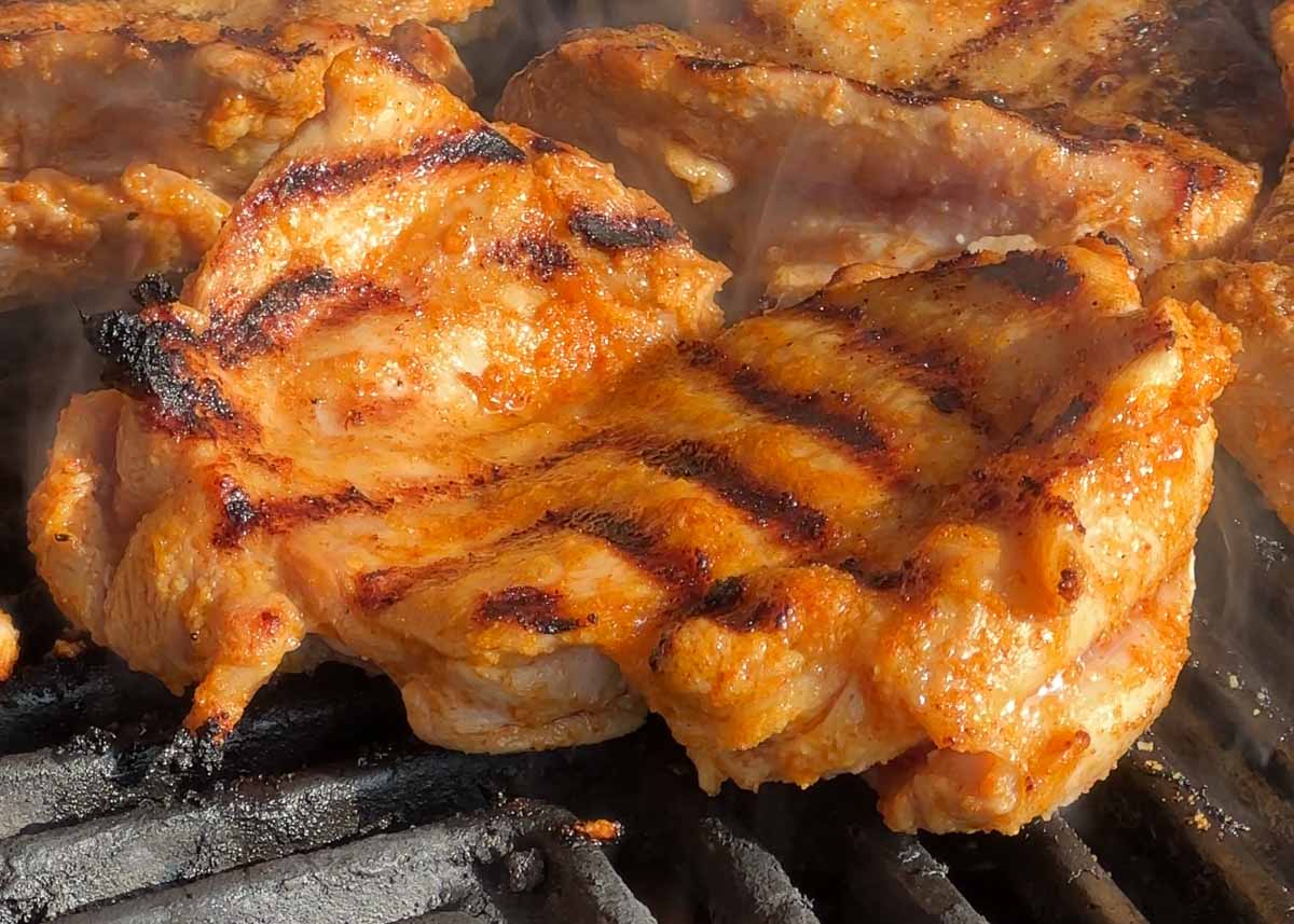 Chicken thighs grilling on a barbecue until charred and cooked through