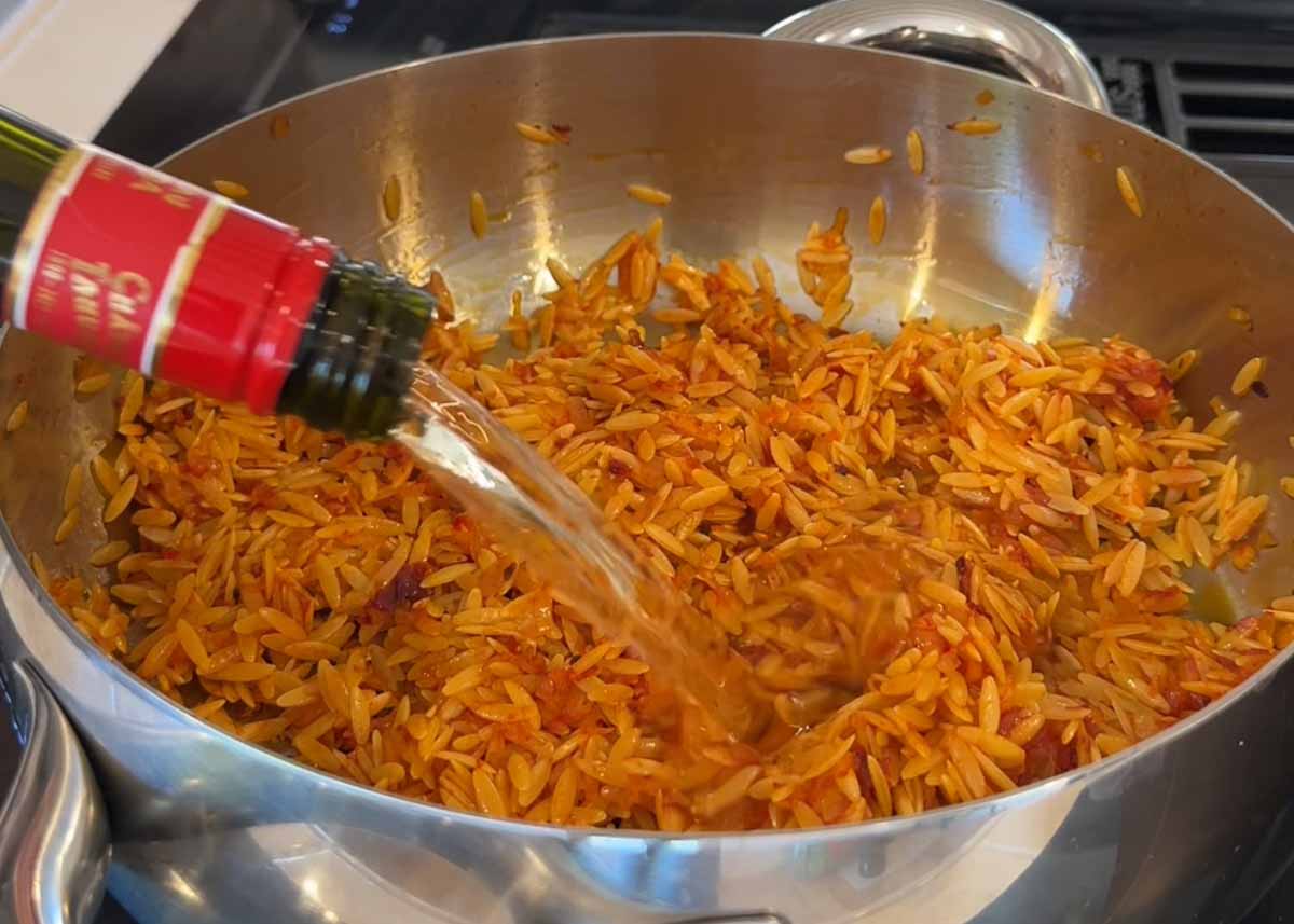 Orzo being deglazed with white wine in pan