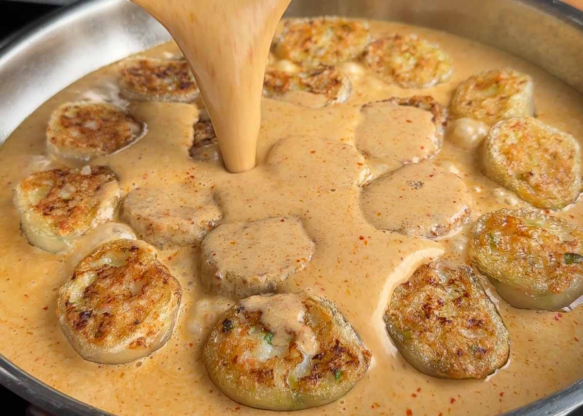Thai red curry sauce being poured over crispy prawn dumplings in a pan