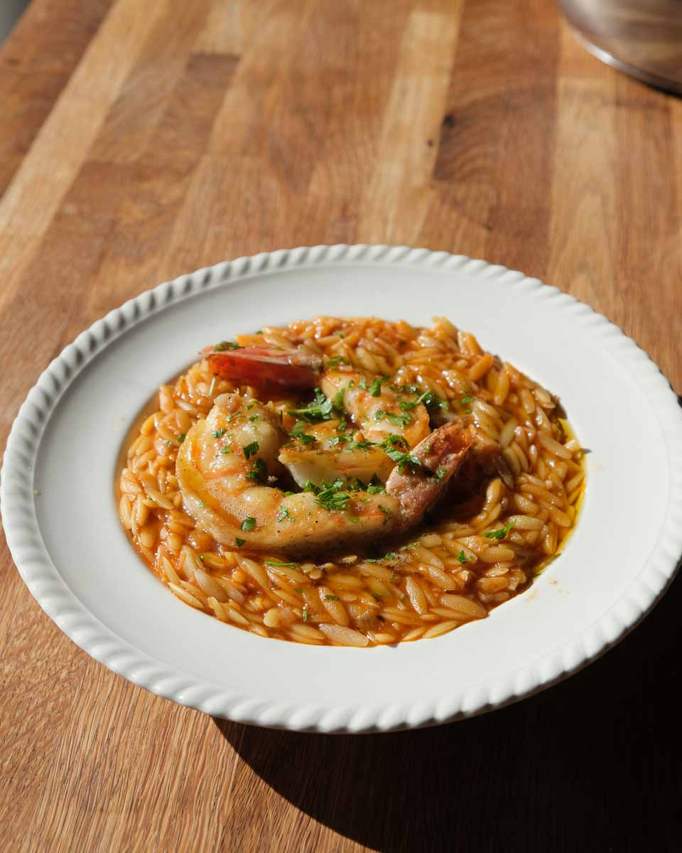 Close up of glossy saffron prawn orzo with parsley and lemon