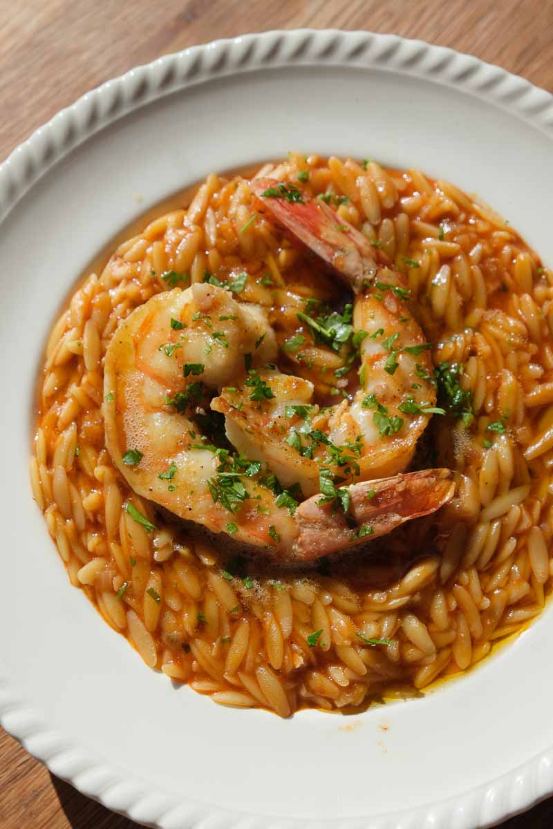 Saffron king prawn orzo served in a bowl with large prawns and fresh herbs