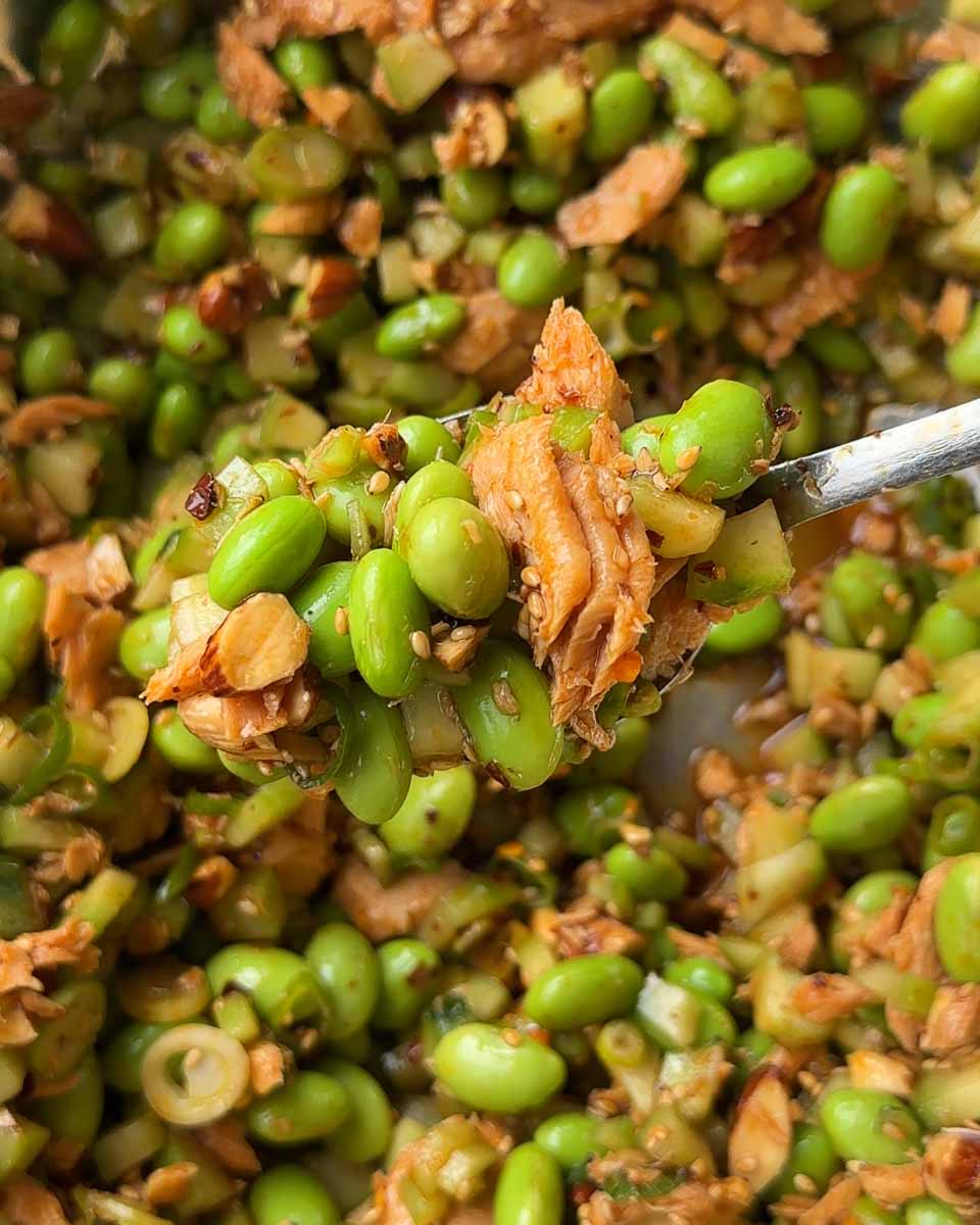 Salmon, edamame and cucumber salad being mixed together in a bowl
