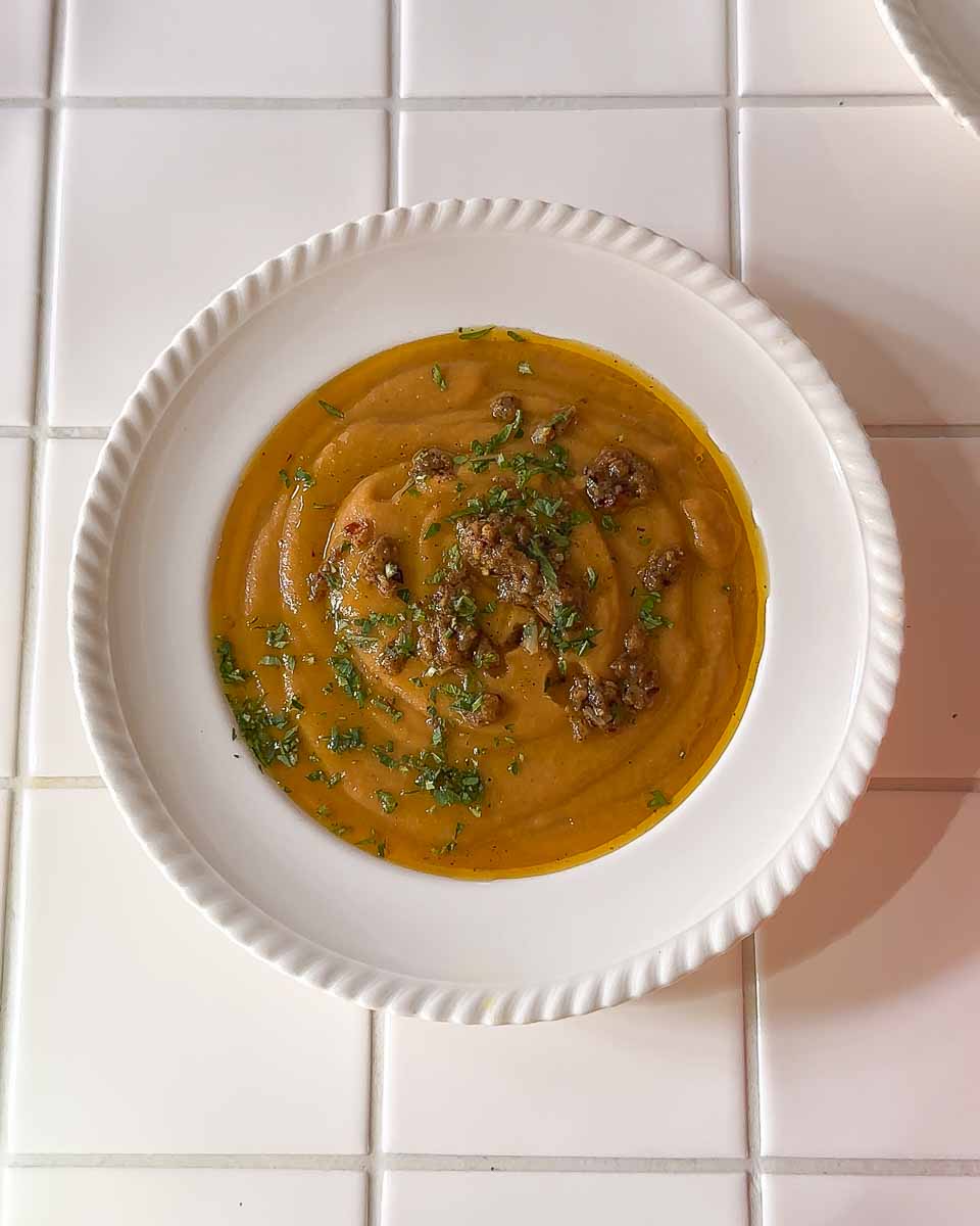 Serving of roasted pumpkin and sweet potato split pea soup in a bowl with herbs