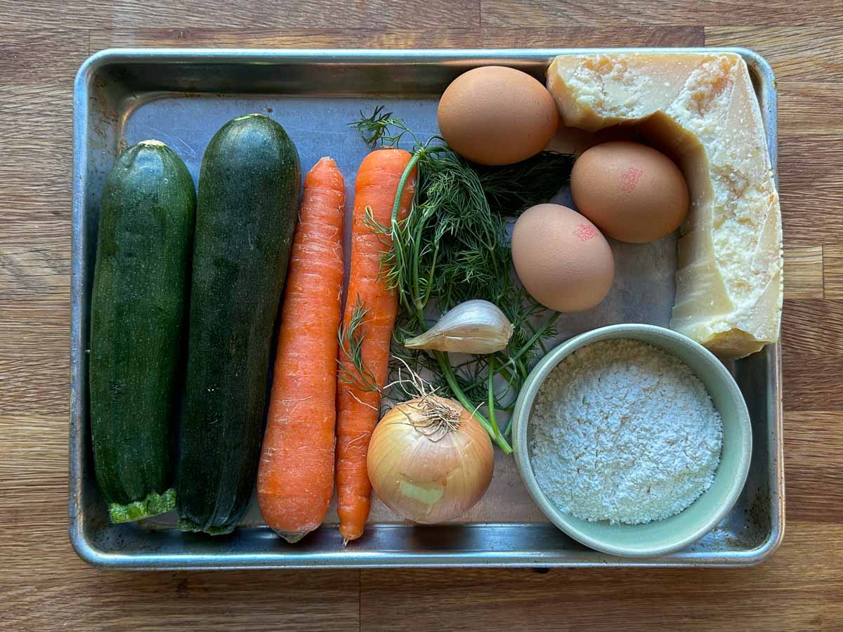 Ingredients for zucchini, carrot and parmesan fritters including fresh vegetables, eggs and herbs
