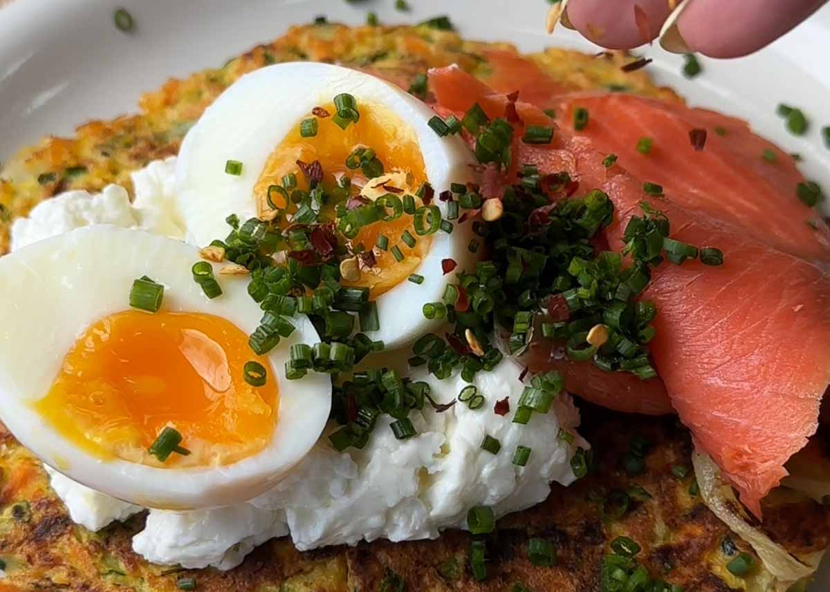 Zucchini carrot parmesan fritters topped with smoked salmon poached egg herbs and chilli flakes
