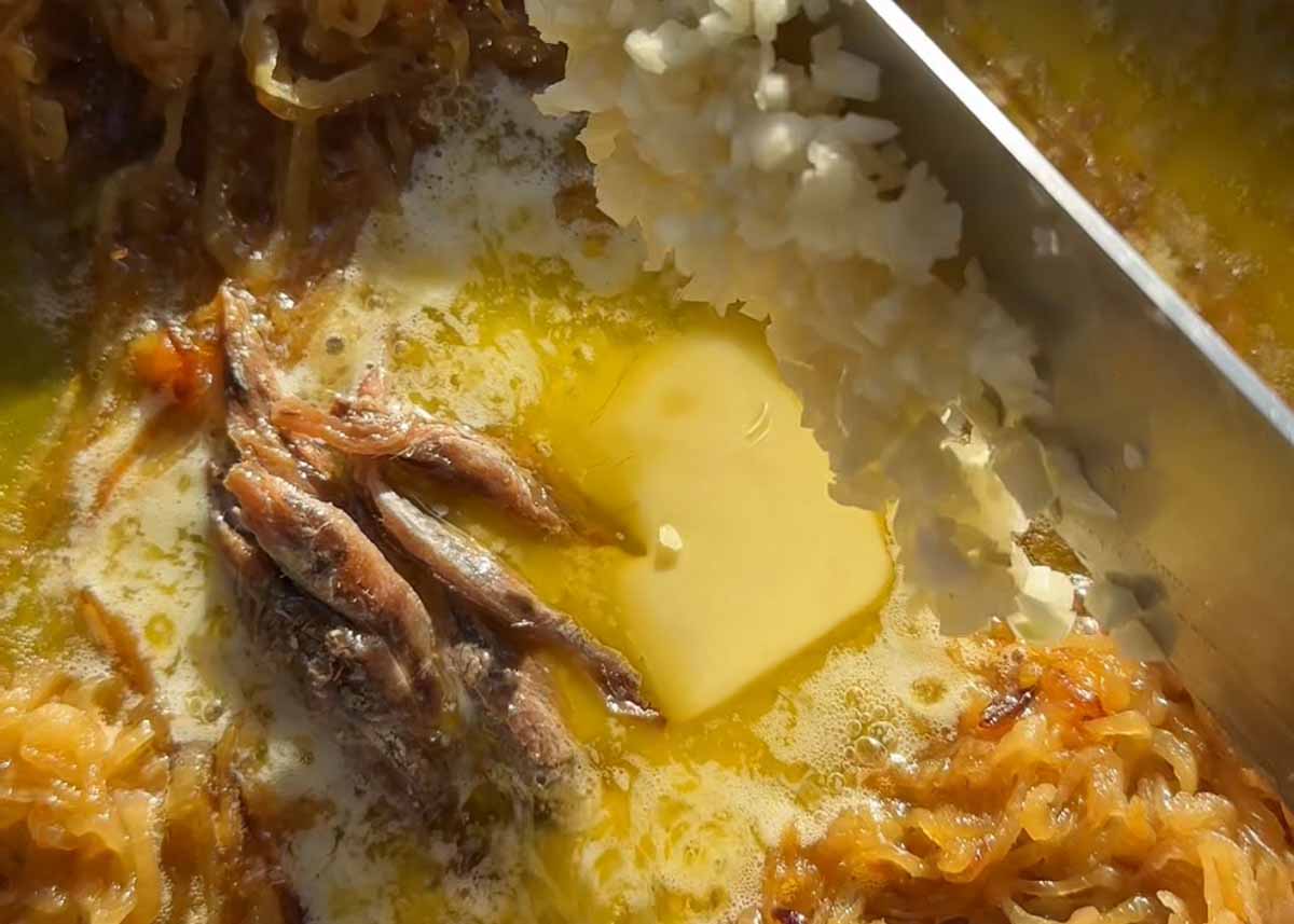 Anchovies melting into caramelised onions with butter in a frying pan