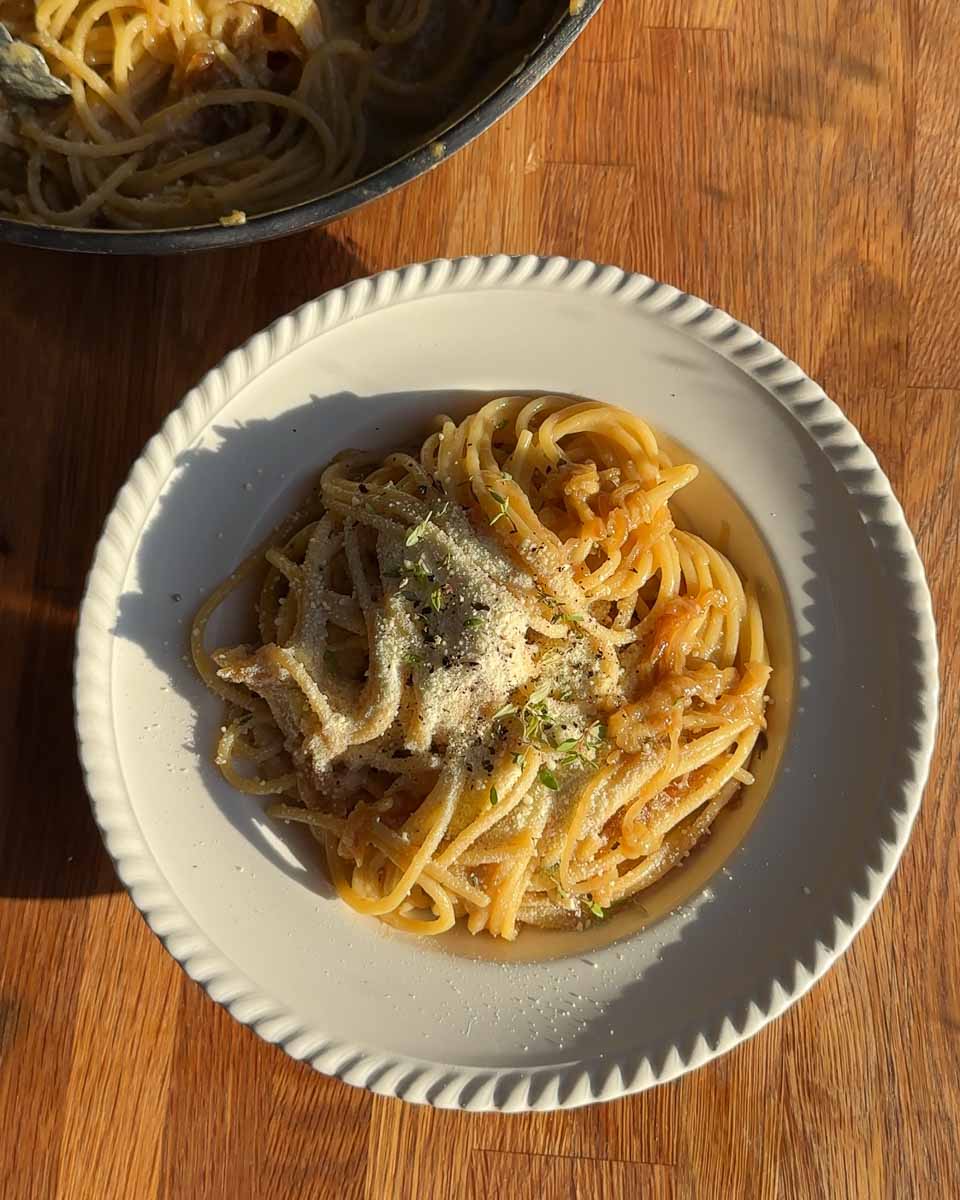 Bowl of caramelised onion and anchovy spaghetti topped with grated parmesan