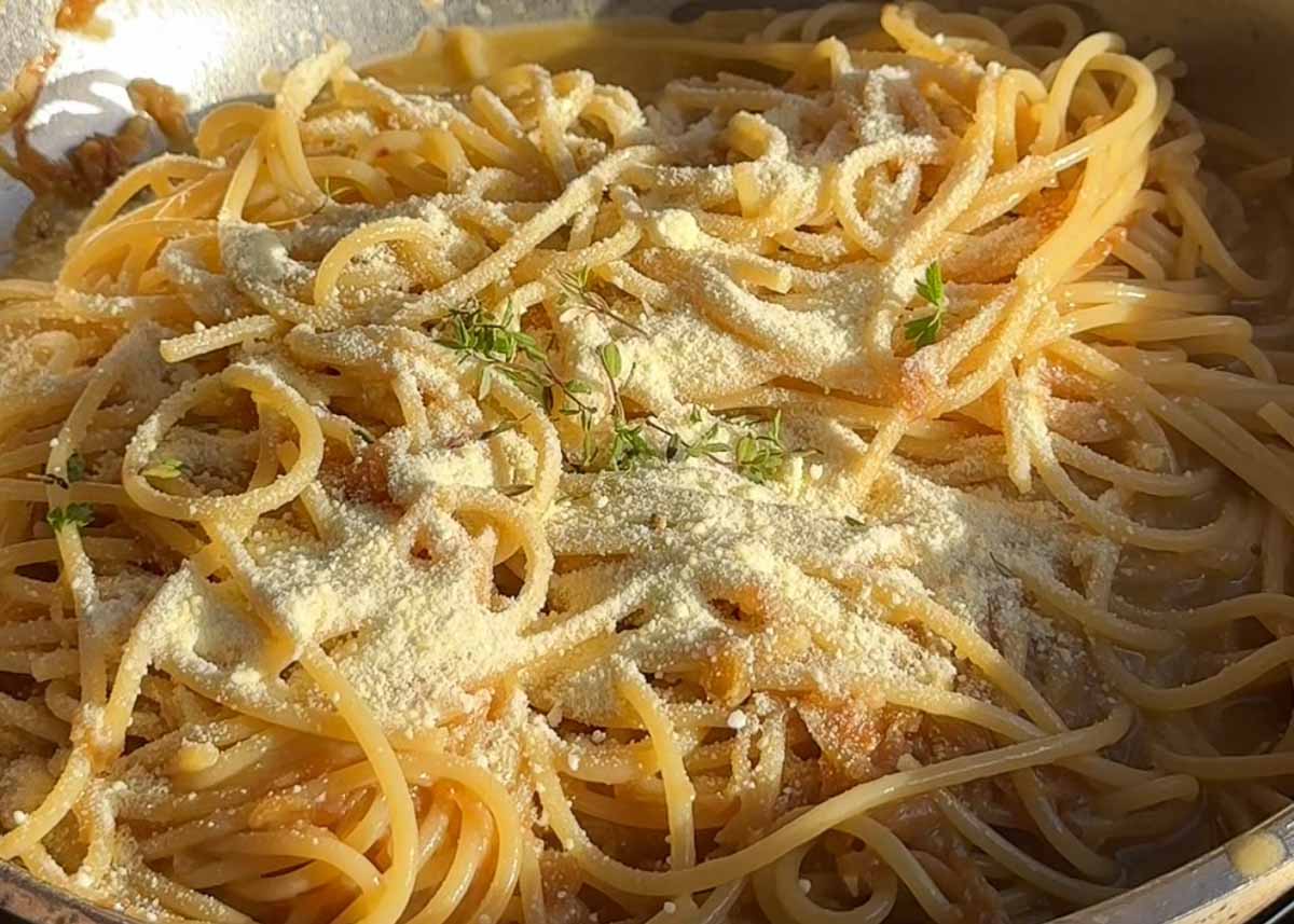 Caramelised onion and anchovy spaghetti in pan with parmesan and black pepper