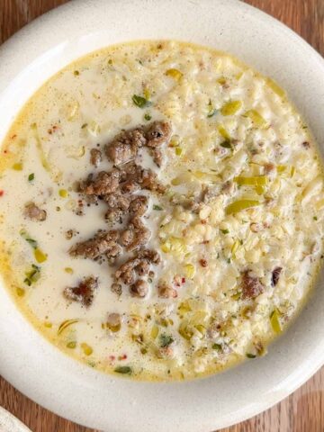 creamy pork and fennel sausage pasta soup in a white bowl with alphabet pasta and crispy sausage