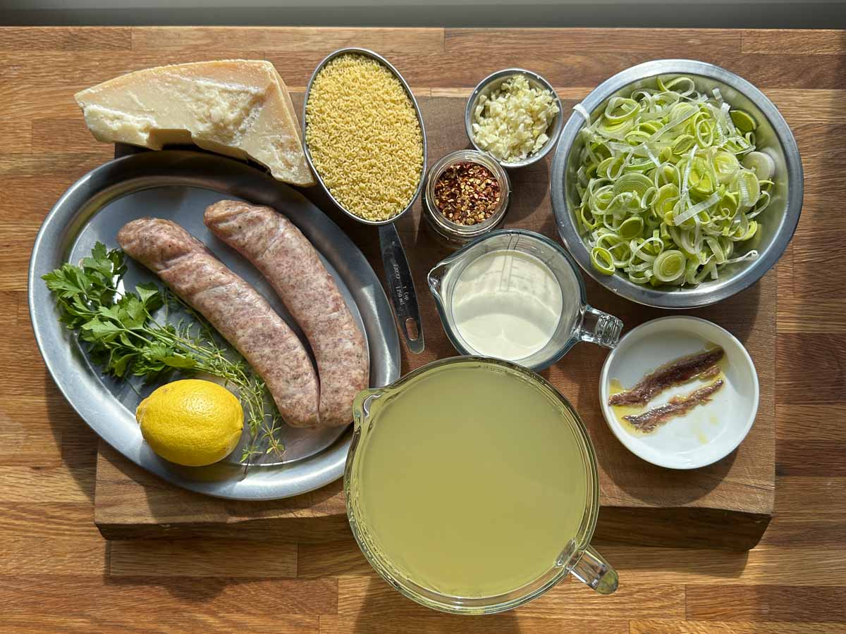 ingredients for creamy pork and fennel sausage pasta soup including sausages leek garlic stock and pasta