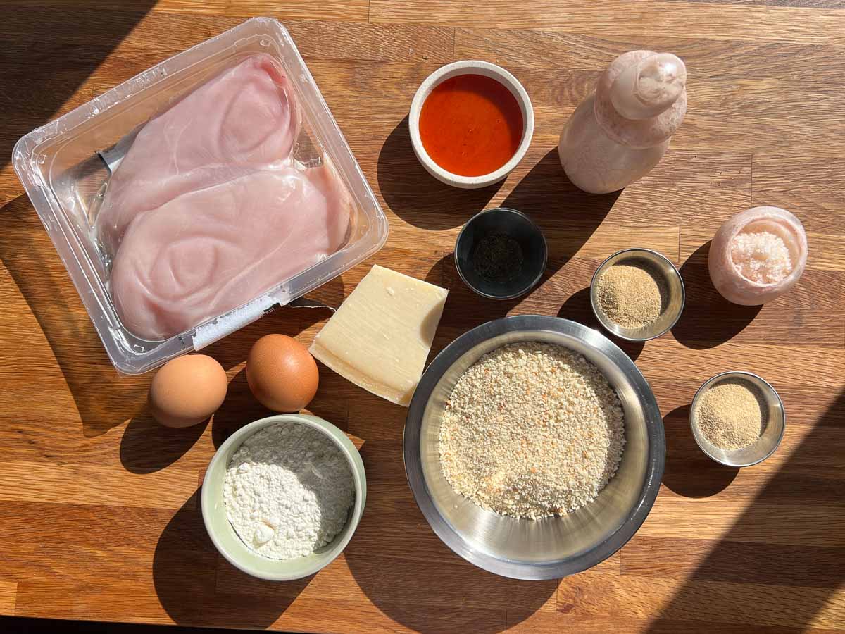 ingredients for hot honey parmesan crumbed chicken including chicken breast, bread crumbs, eggs, hot honey, garlic powder, onion powder, thyme, salt and pepper