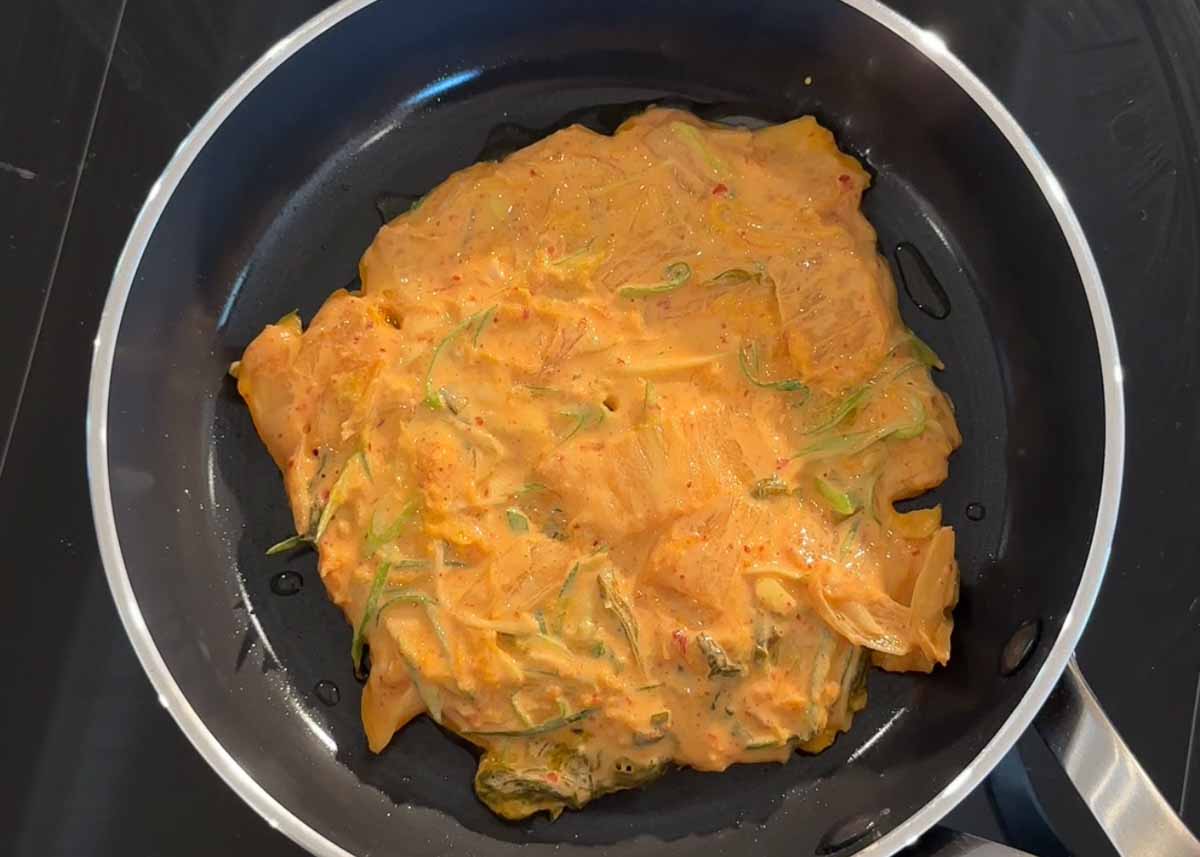 Kimchi pancake cooking in a pan until crispy and golden