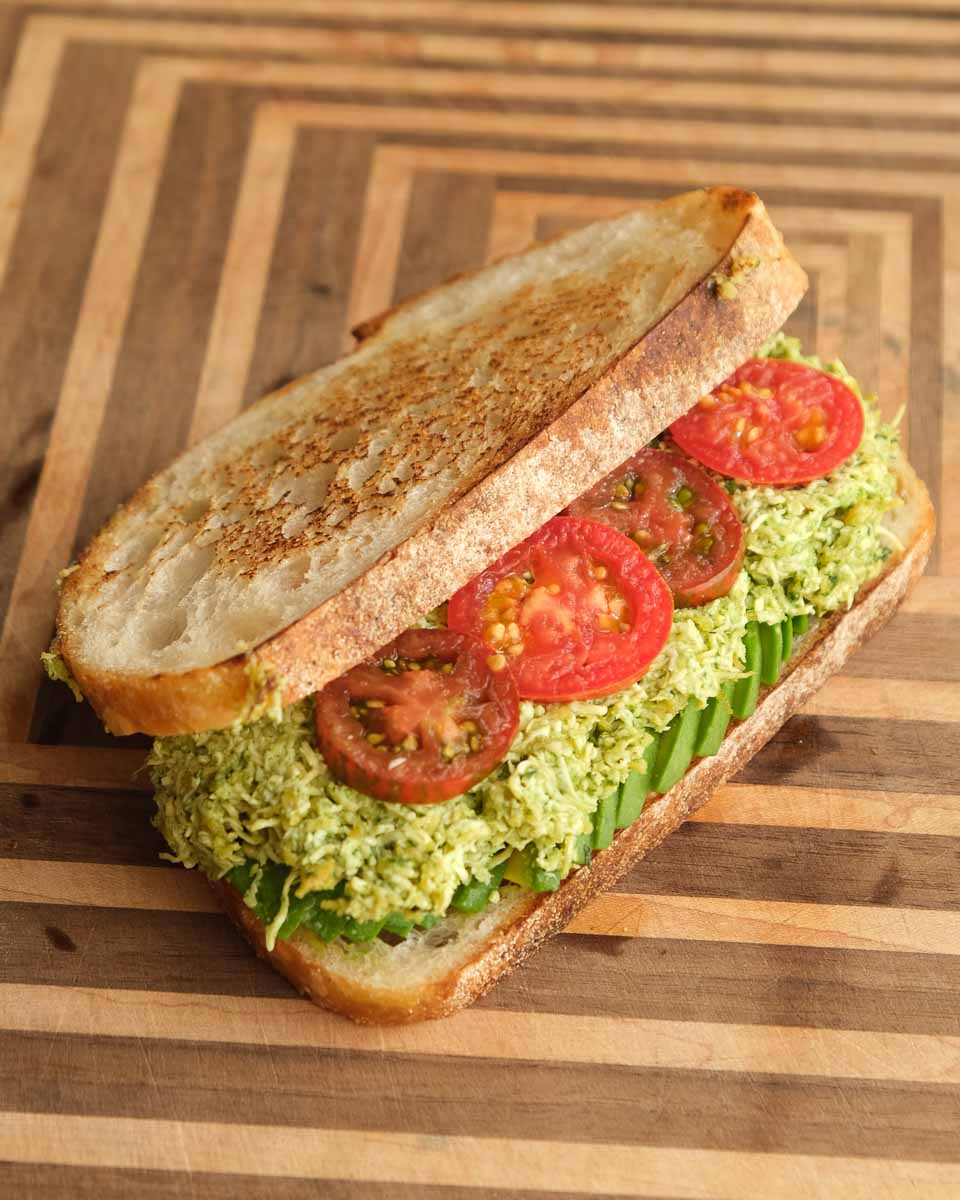 Assembling tofucado sandwich with pesto, tofu avocado filling and tomato slices