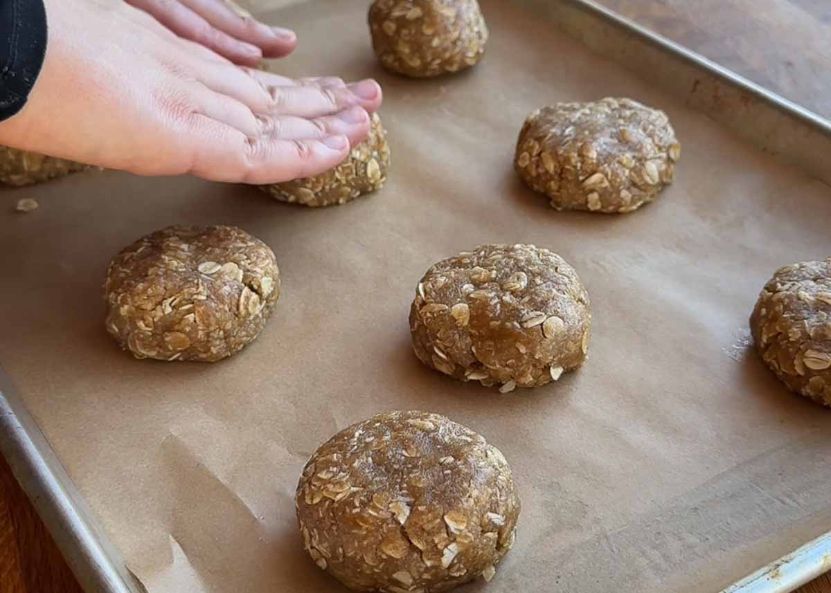 rolling oat coconut biscuit dough into balls on baking tray before baking