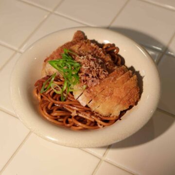 Sweet soy butter udon with crispy panko chicken sliced on top and garnished with spring onion