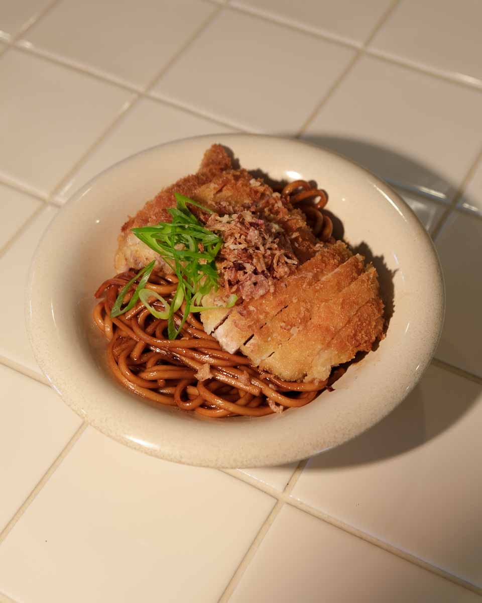Crispy panko chicken served over sweet soy butter udon noodles with spring onion and sesame seeds