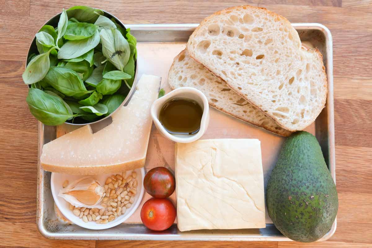 Ingredients for tofucado pesto toasted sandwich including tofu, avocado, bread and fresh herbs
