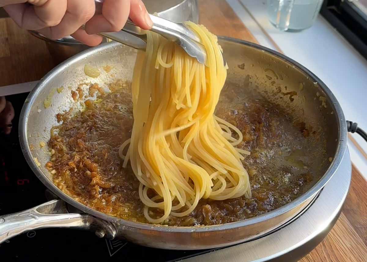 Spaghetti being tossed through caramelised onion and anchovy butter sauce