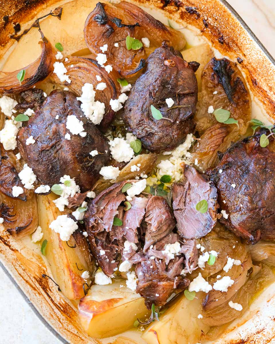 Close-up of pull-apart lamb shanks with golden potatoes and feta.