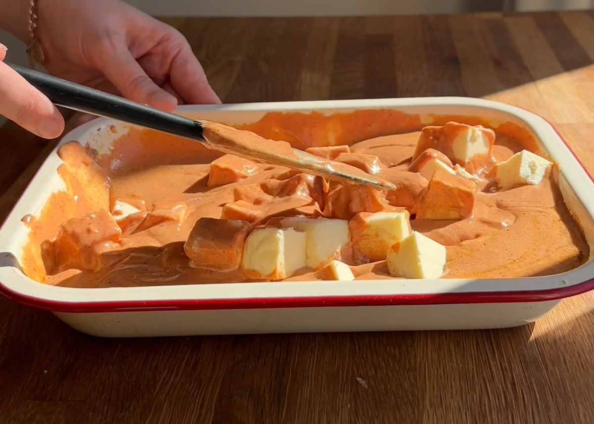 Paneer cubes being mixed into butter paneer sauce in baking tray