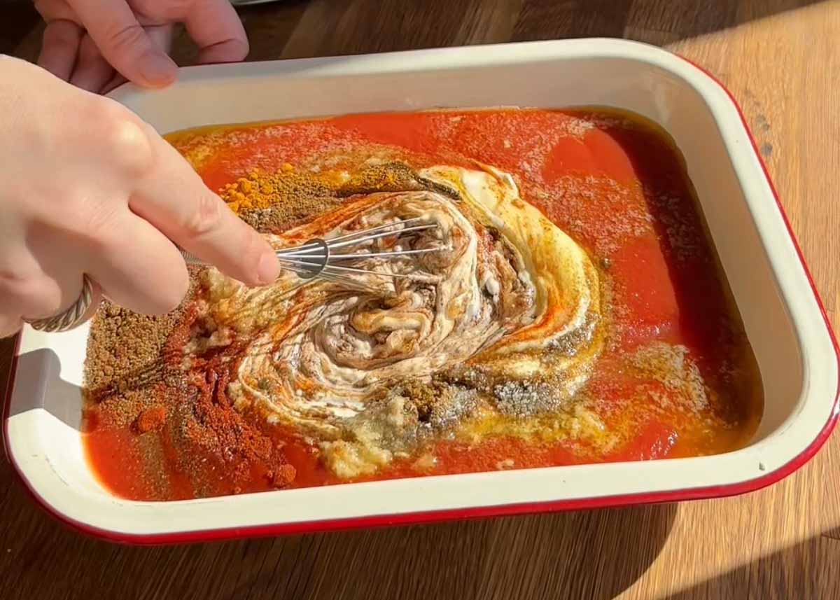 Swirling yoghurt through butter paneer sauce in baking dish before baking