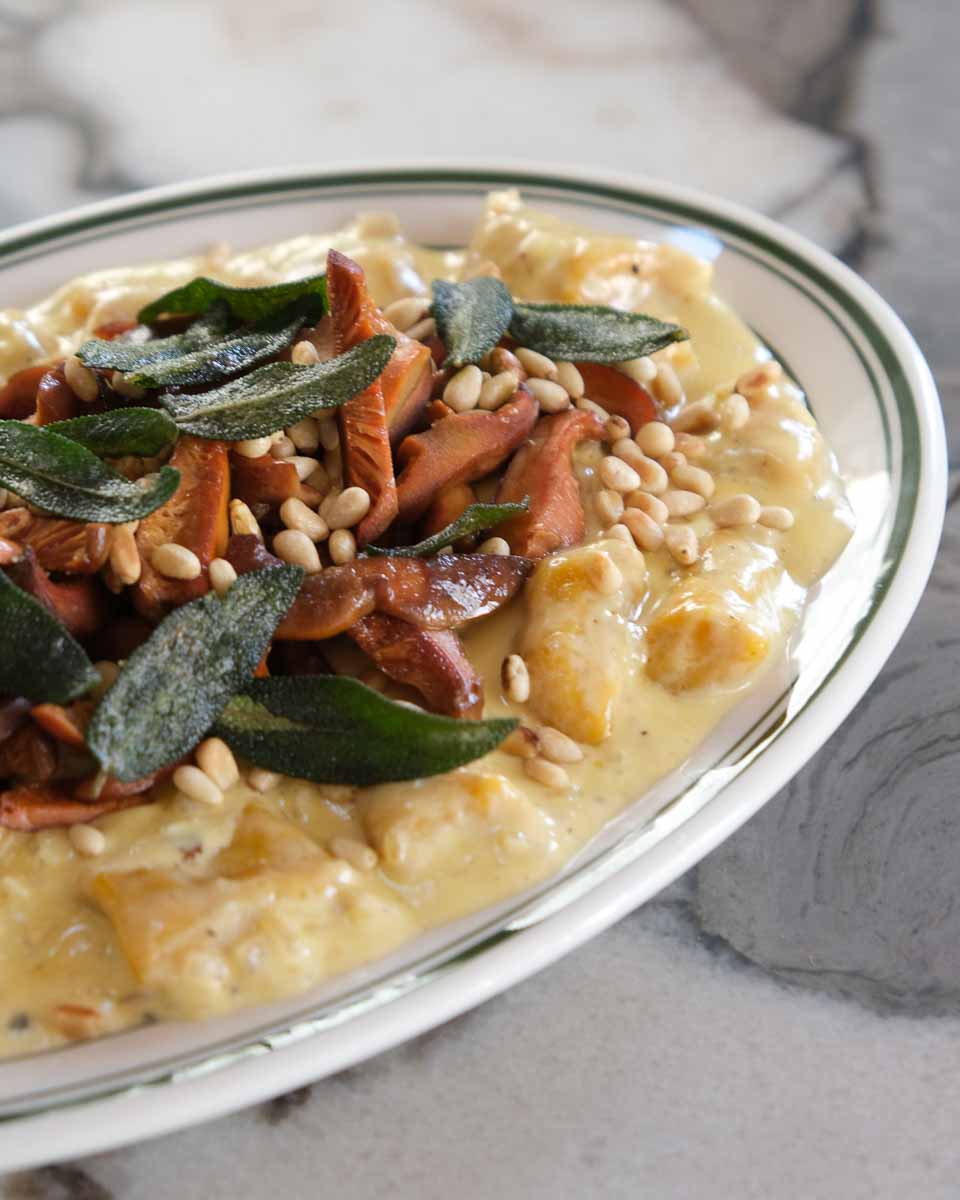 Creamy pumpkin gnocchi with crispy pine mushrooms, sage and toasted pine nuts served on a plate