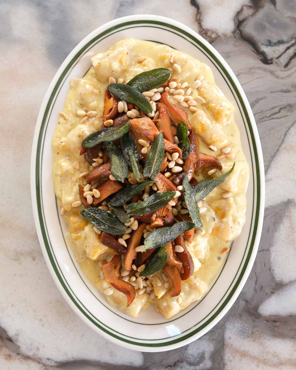 Creamy pumpkin gnocchi with crispy pine mushrooms, sage and toasted pine nuts served on a plate