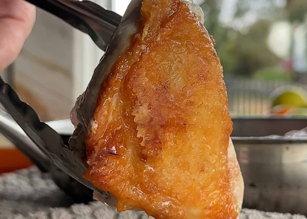 Crispy browned chicken thigh skin being rendered in a frying pan for miso chicken rice bake.