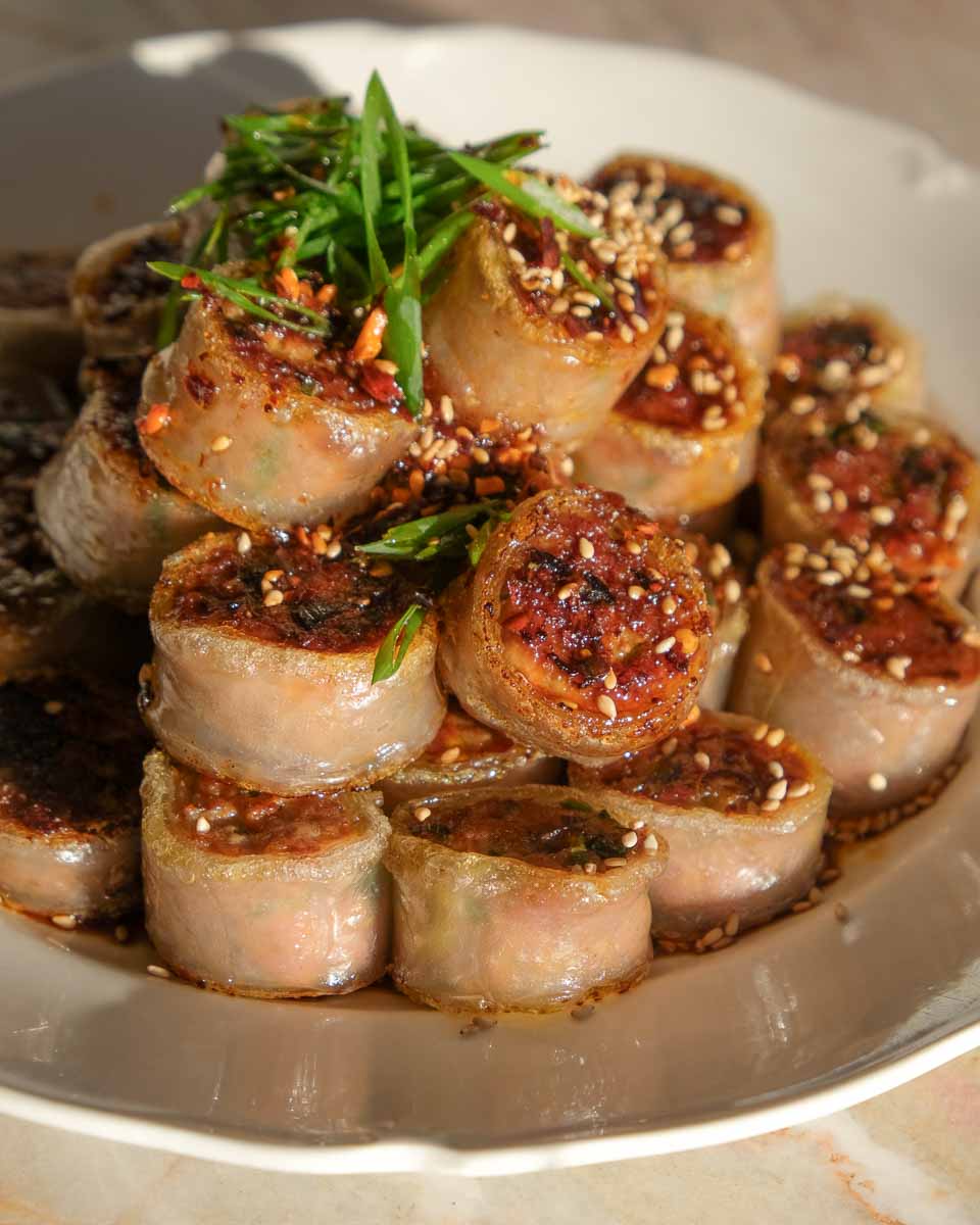 Stacked crispy rolled pork rice paper dumplings garnished with fresh herbs.