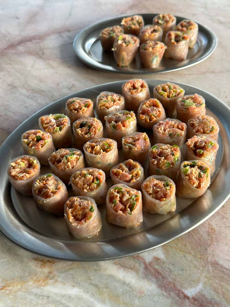 uncooked rolled pork rice paper dumplings on plate ready to be cooked