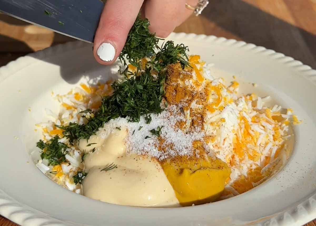 Curried grated egg mixture with mayonnaise and herbs being mixed