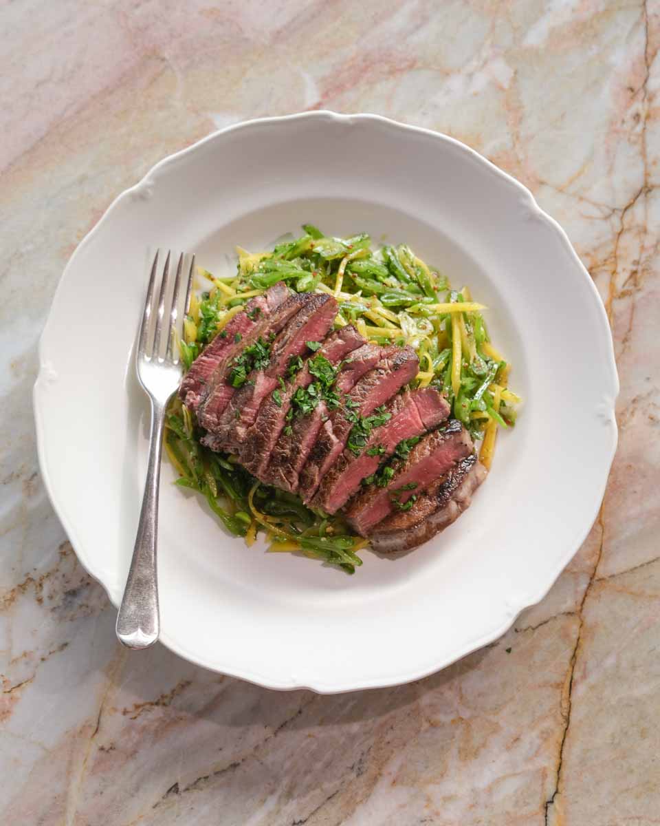 Eye fillet steak plated with fresh sliced snow pea salad and herbs