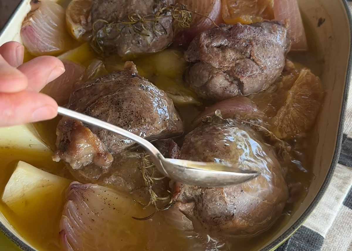 Boneless lamb shanks braising in stock with potatoes and onion.
