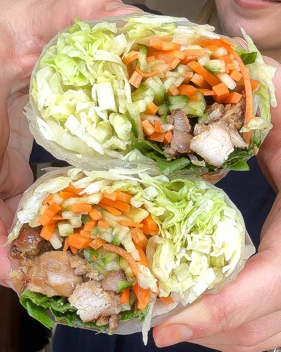 Close up of lemongrass chicken rice paper burritos filled with pickled vegetables, lettuce and herbs.