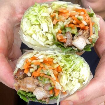 Handheld lemongrass chicken rice paper burritos showing the fresh filling inside.
