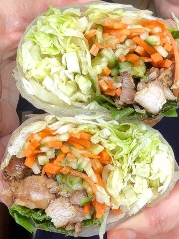 Handheld lemongrass chicken rice paper burritos showing the fresh filling inside.