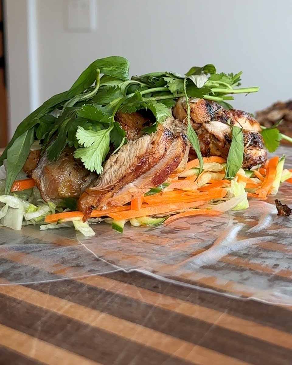Lemongrass chicken rice paper burritos served on a wooden board with fresh herbs.