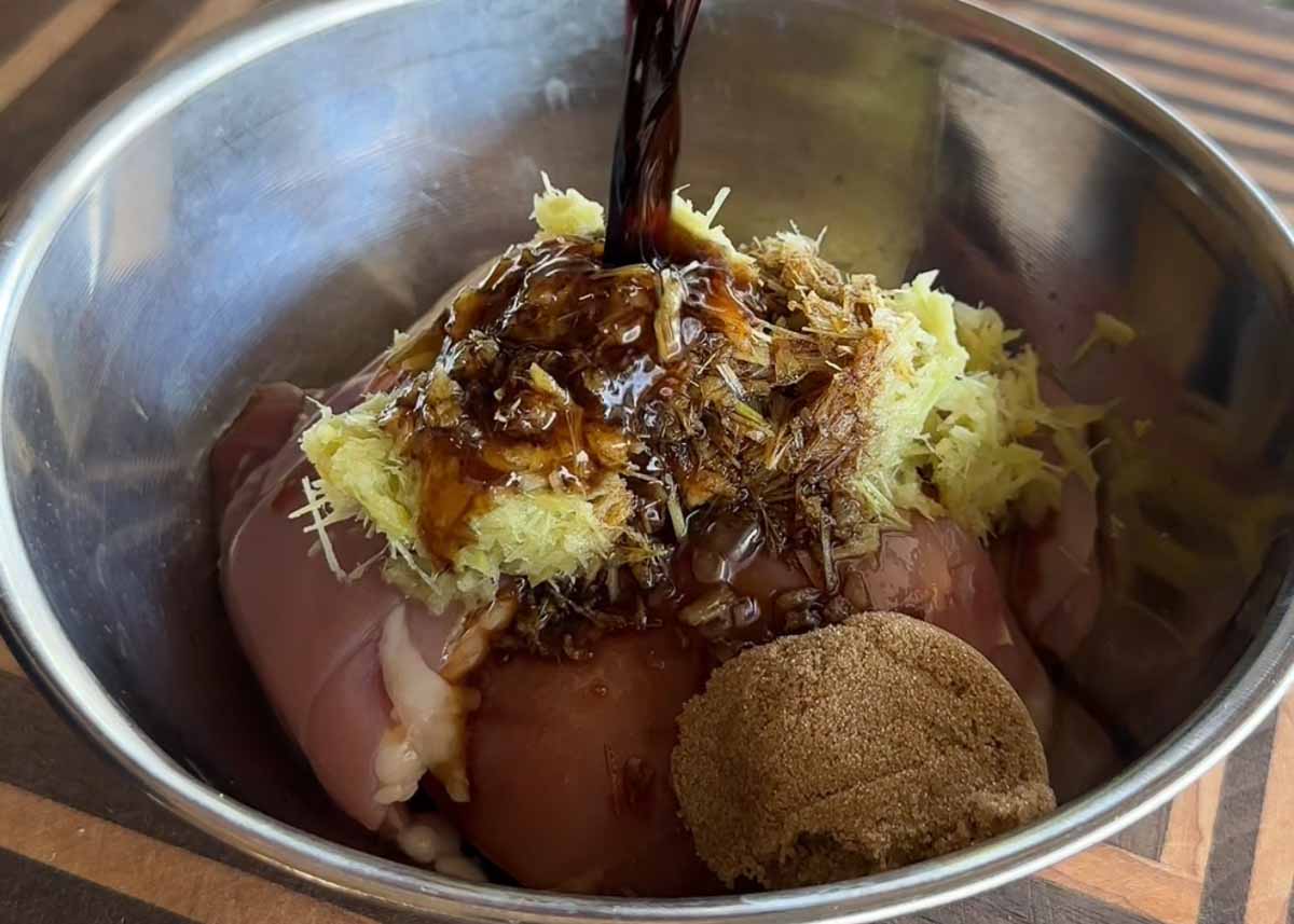Chicken thighs marinating with lemongrass, garlic, ginger and sauces in a bowl.