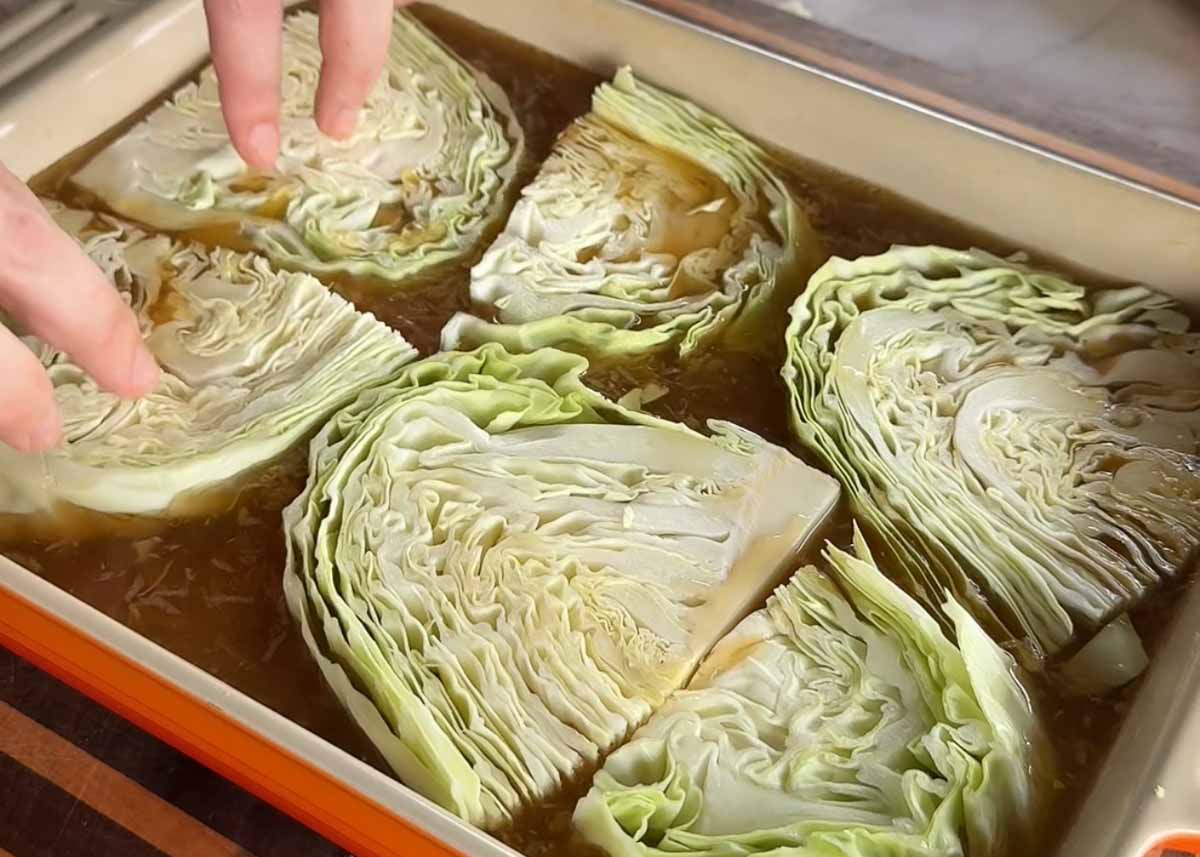 Green cabbage wedges layered over seasoned rice in a baking tray.