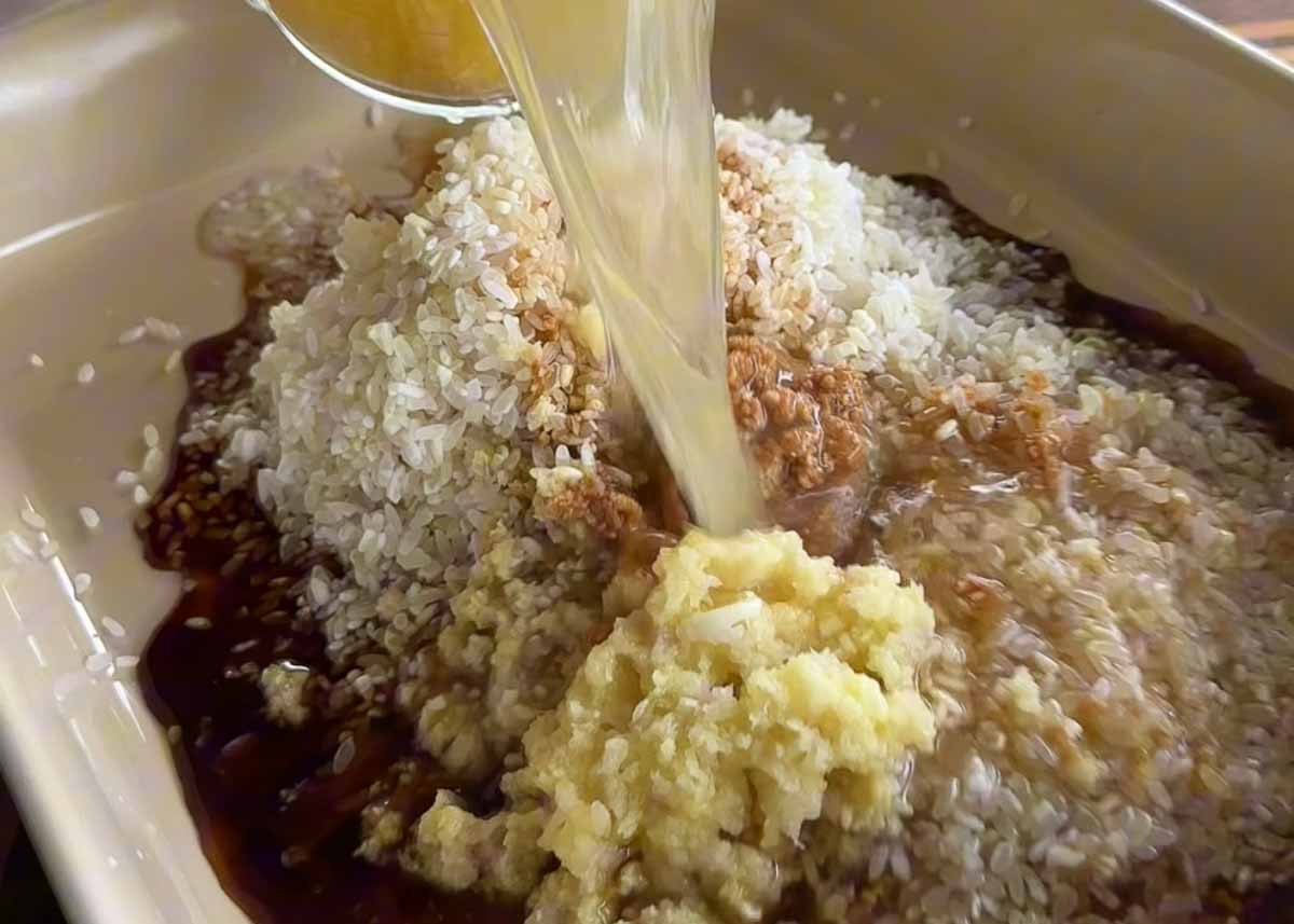 Rice, stock, garlic and miso being added to a baking dish for one tray chicken rice bake.